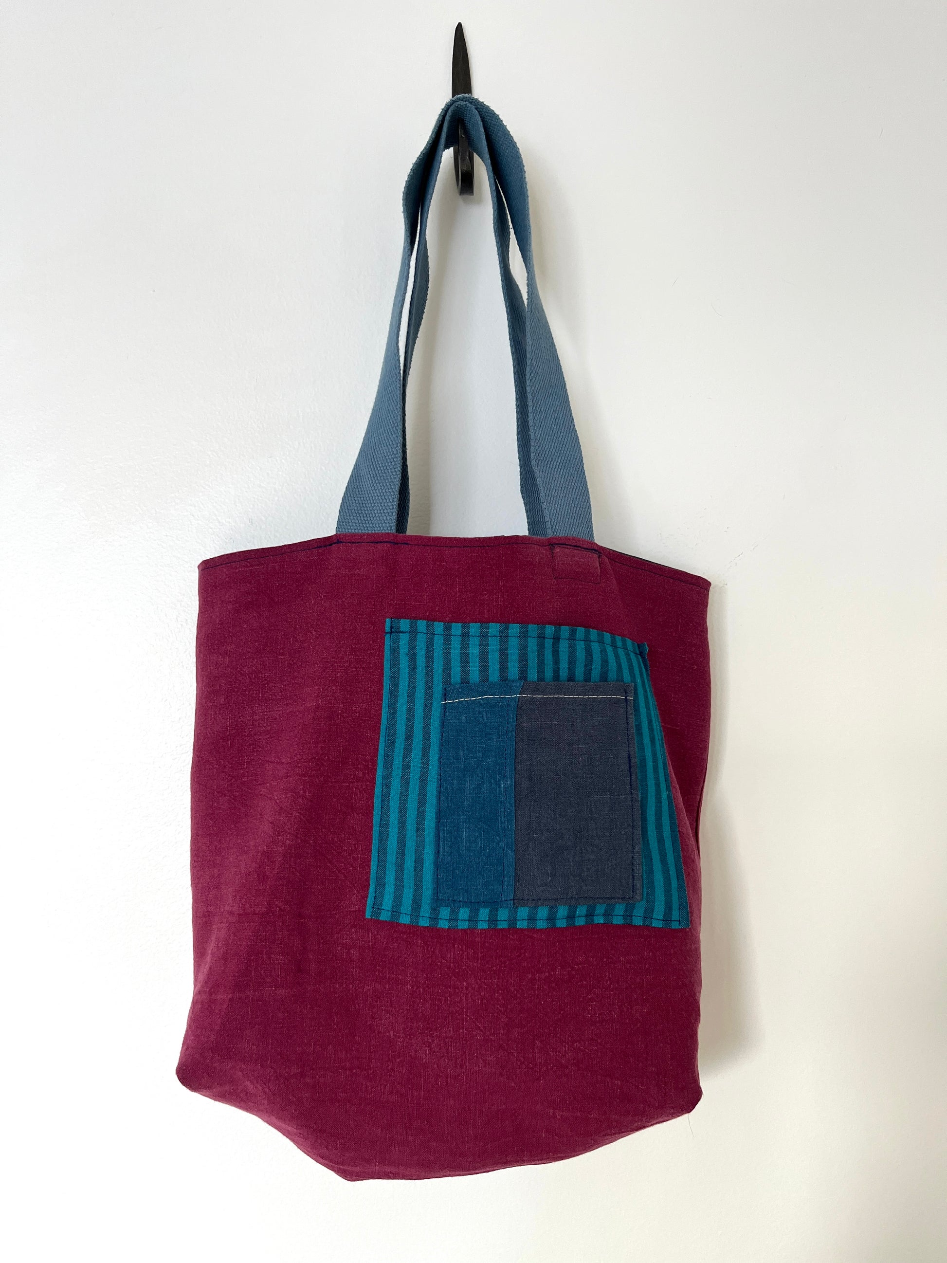 The burgundy side of a reversible linen tote bag showing the striped pockets.