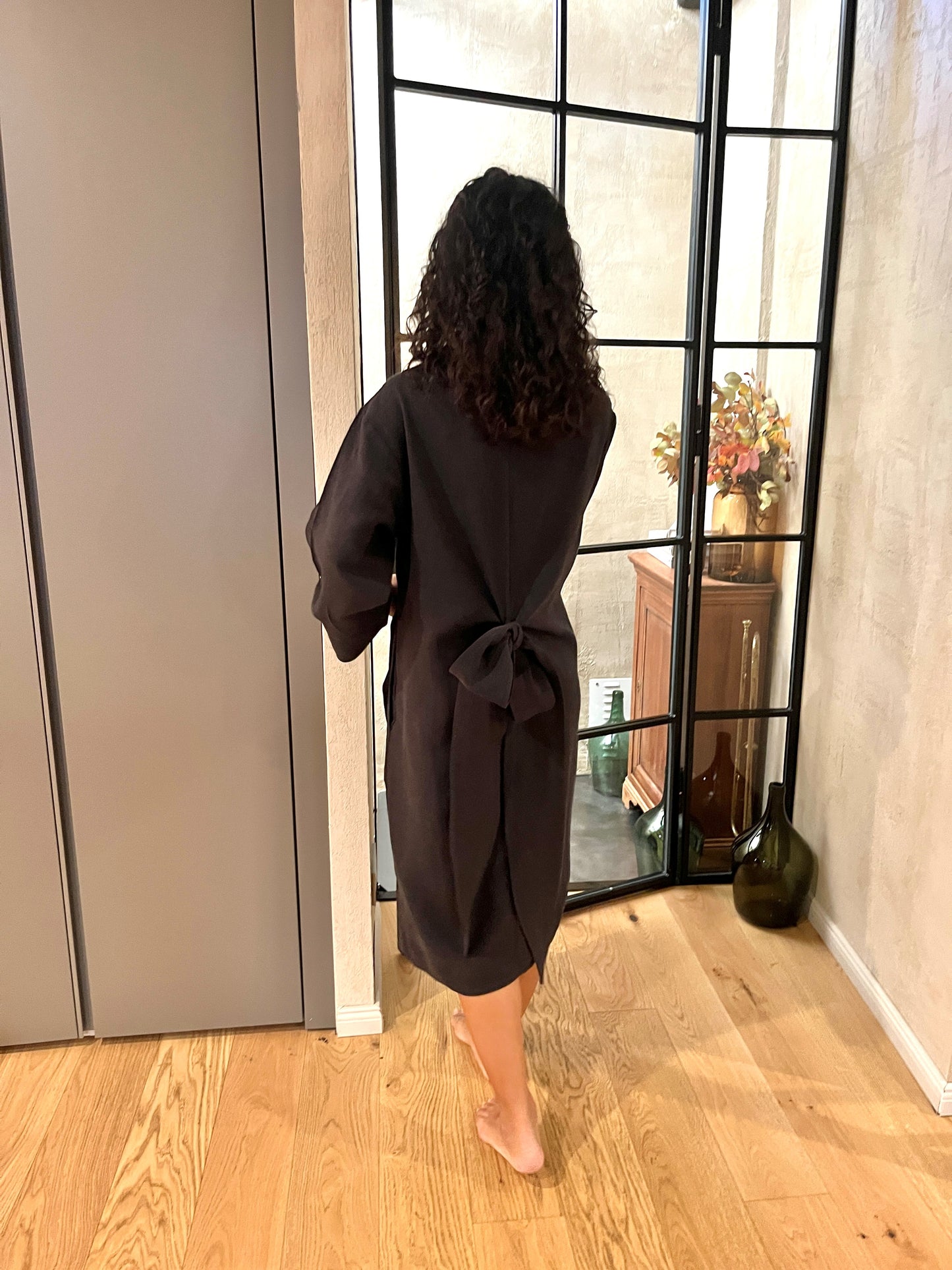 View from behind of a woman in a black linen robe, opening a French door. 