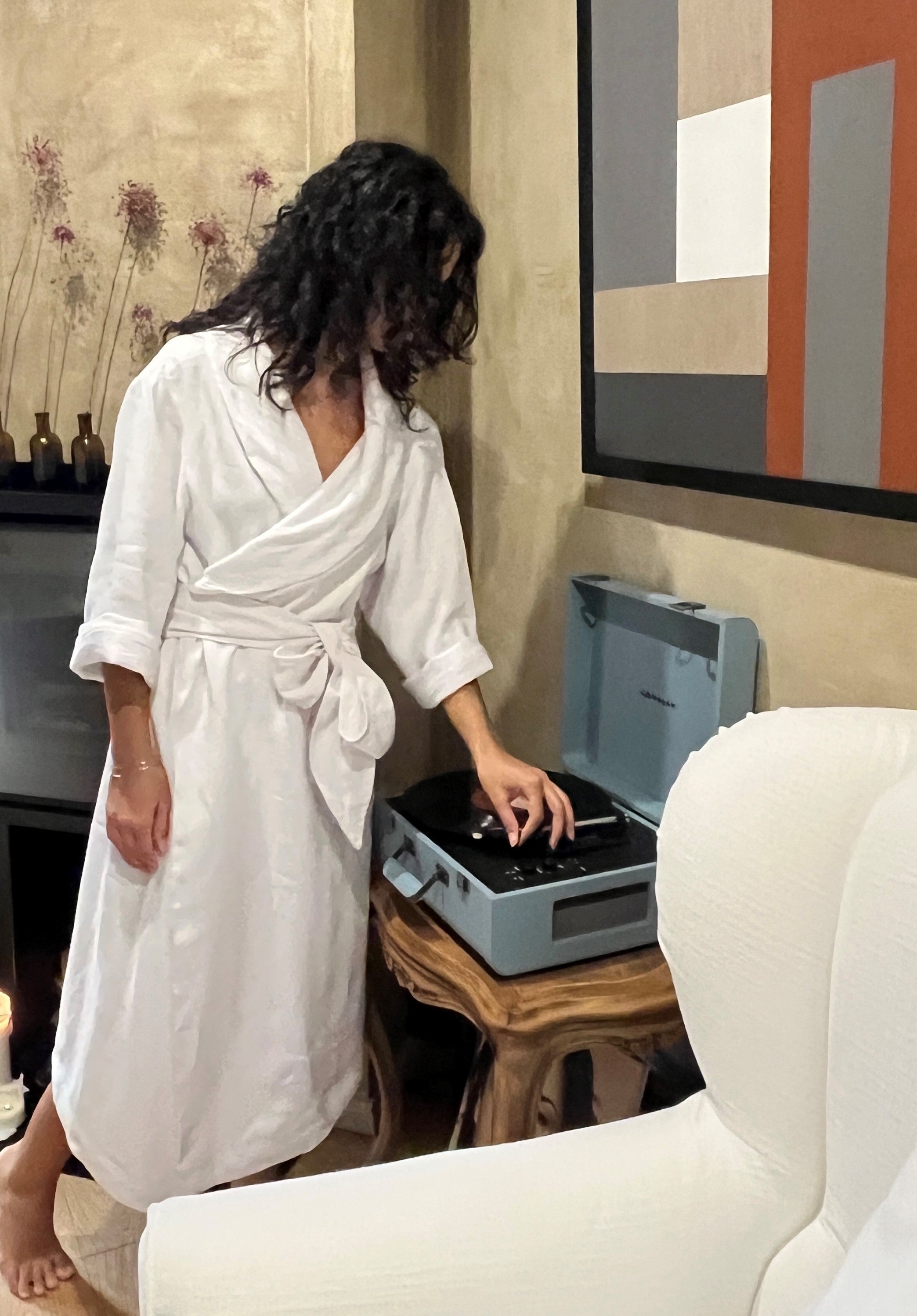 Woman starting to play a record, wearing our white linen robe.