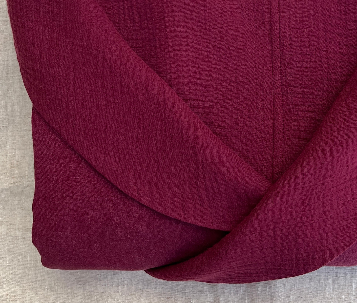 Close up photo of a folded burgundy linen robe with an organic cotton double gauze lining.